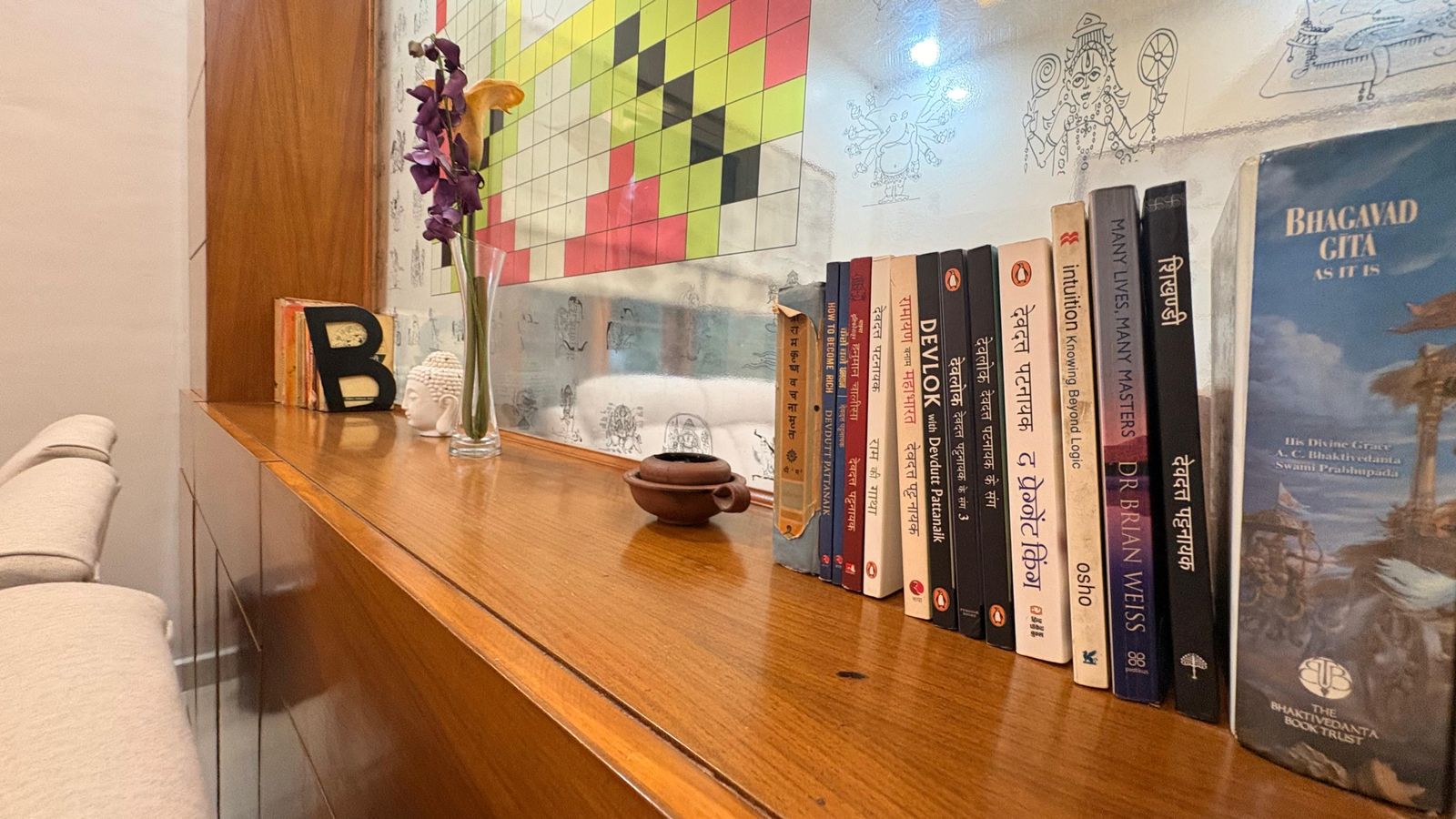 A long wooden console holding the practice’s working library — the Bhagavad Gita among the other volumes.